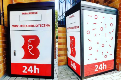 Wrzutnia biblioteczna. Biało-czerwona. Od przodu logo biblioteki - czerwone B, z białą syrenką warszawską w środku. Napis: Wrzutnia biblioteczna, 24h, na górze napis: tutaj wrzuć. Od boku dekoracja w formie rozsypanki elementów, takich samych, z jakich złożona jest syrenka.